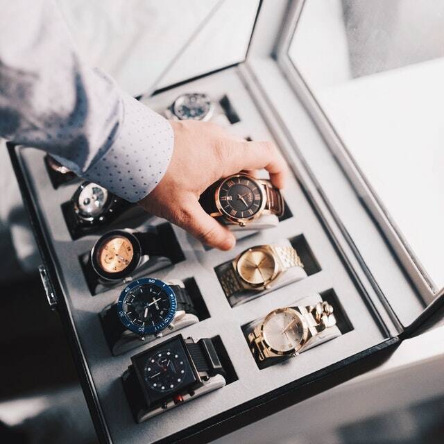 A man putting watches in a case on a bed.