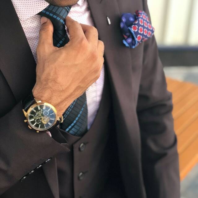 A man in a brown suit is adjusting his tie.