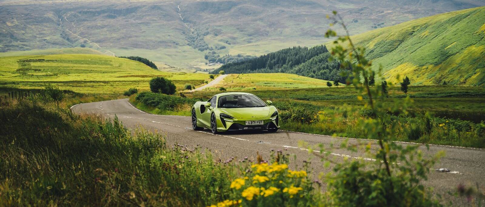 A green mclaren sports car driving down a country road.