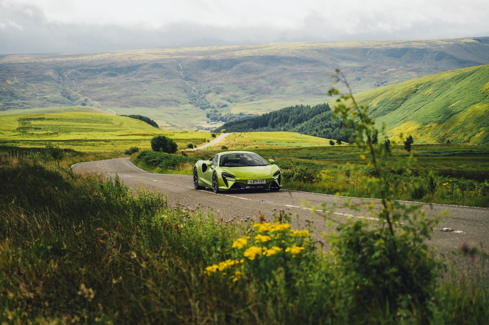A green mclaren sports car driving down a country road.