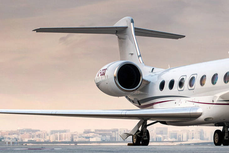 A private jet sitting on the tarmac with a city in the background.