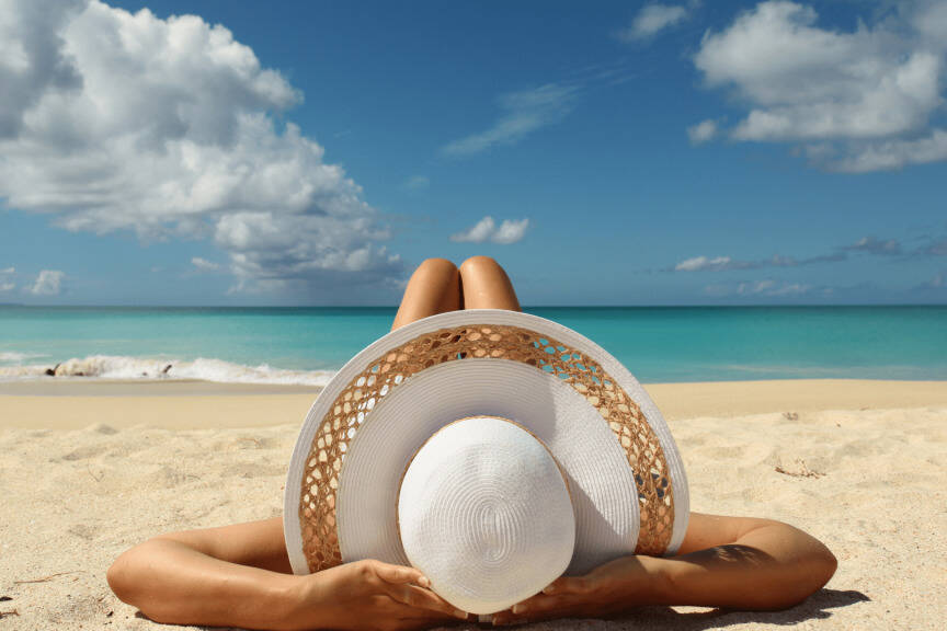 A woman laying on the beach with a white hat.