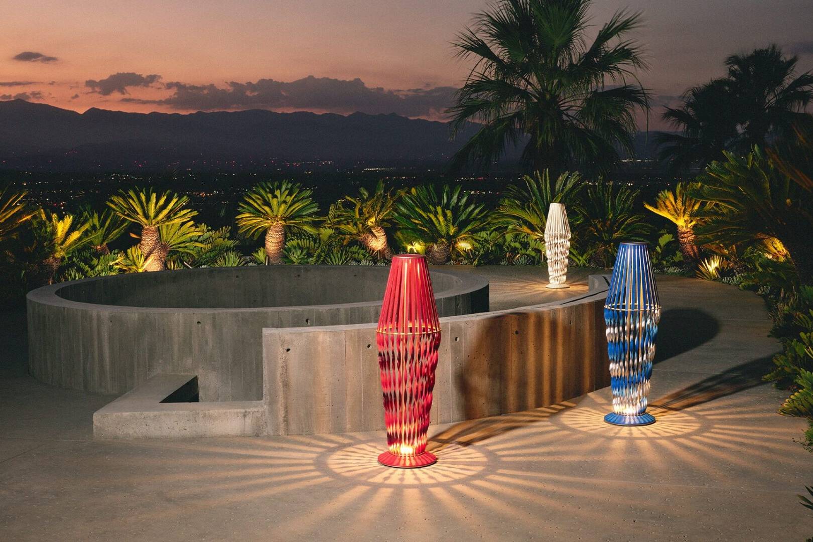 Three colorful glass vases are lit up at dusk.