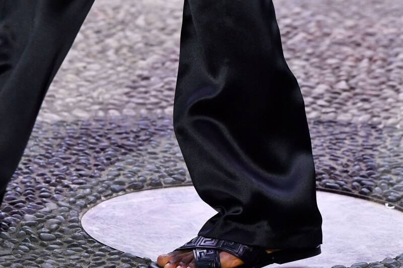 A person wearing black pants and sandals on a runway.
